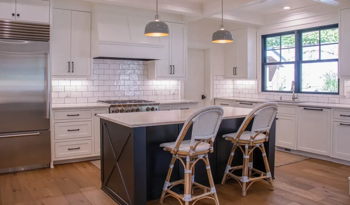 A white-cabinet kitchen after a rewire, with enamel pendants over the island, under-cabinet lighting and new receptacles along the tile backsplash